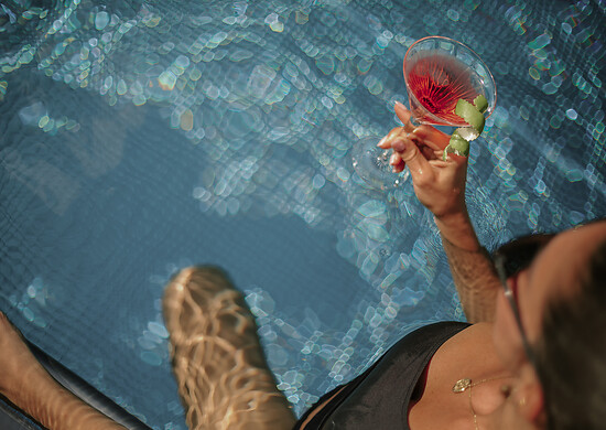 Frauenhand hält Drink am Pool mit Limette