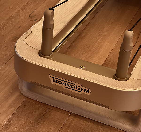Nahaufnahme eines Pilates-Reformers der Marke 'TECHNOGYM' auf einem Holzfußboden.