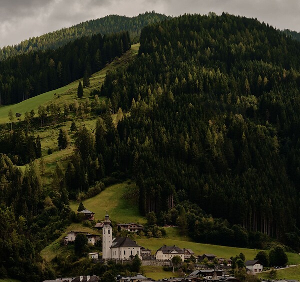 Ein Bergdorf mit Kirche und mehreren Häusern am Fuß eines bewaldeten Hügels.