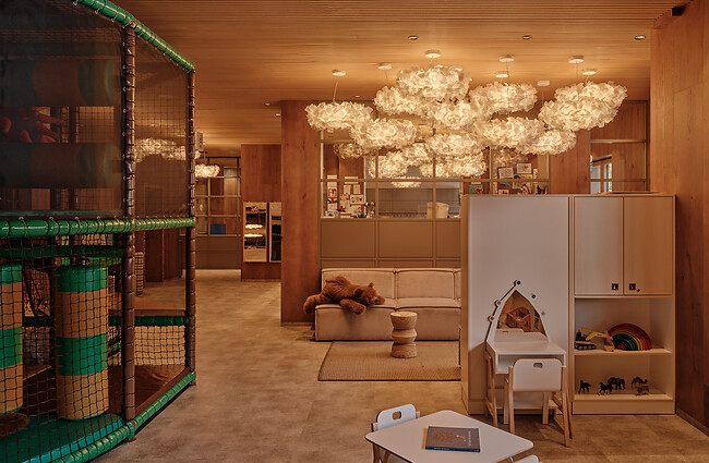 Eleganter Spielbereich für Kinder mit Lounge-Möbeln, warmem Licht, dekorativem Kronleuchter und Spielzeug.