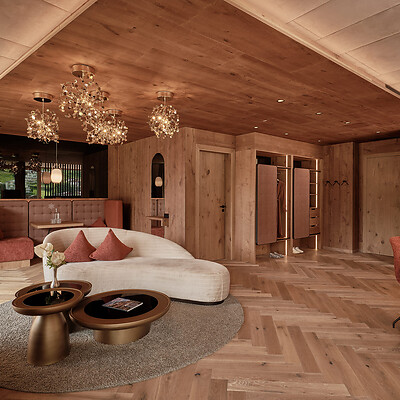 Wohnzimmer mit geschwungener weißer Couch, zwei runden Couchtischen auf grauem Teppich und mehreren Kronleuchtern an der Holzdecke.