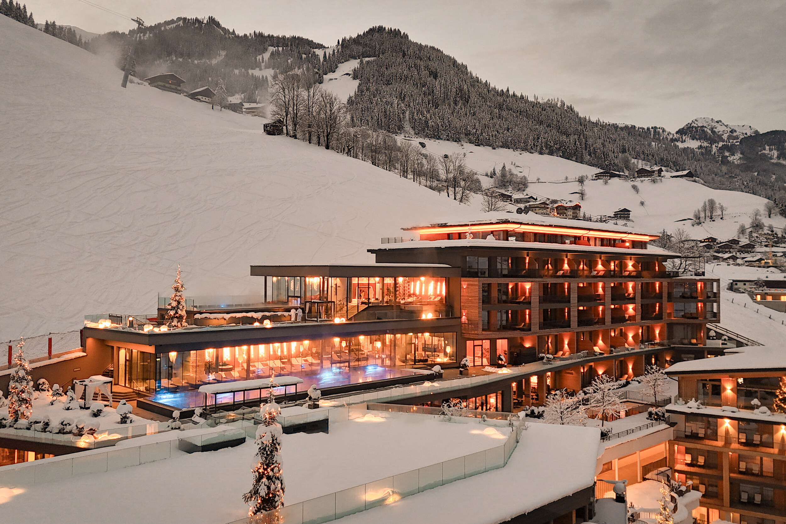 Beleuchtetes Hotelgebäude bei Dämmerung - im Hintergrund schneebedeckte Landschaft.