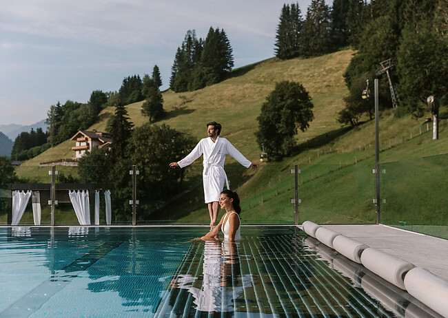 Paar sitzt im Infinity Pool und blickt in die Ferne zu den Bergen