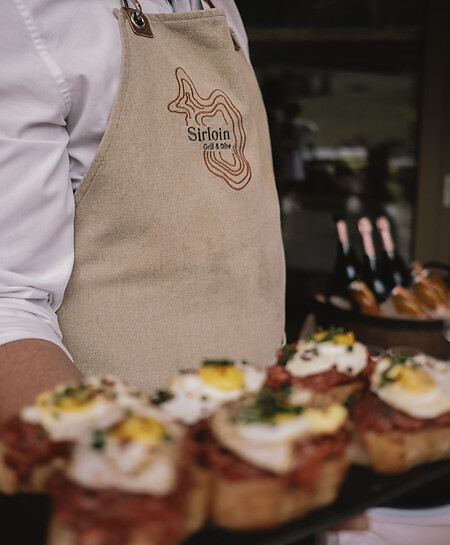 Man serves beef tartare from the Steakhouse Grossarl with an apron from Sirloin Grill & Dine.