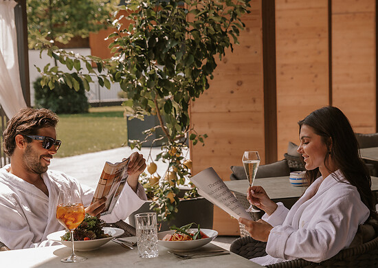Couple sitting in bathrobes enjoying Dolce Vita flair and eating in the garden of the spa hotel austria