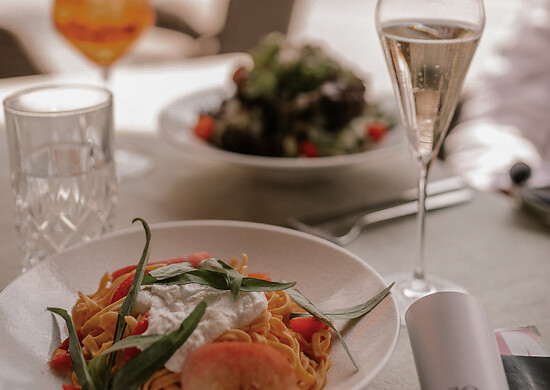 Fresh tagliatelle with burrata and peach and 2 glasses with salad in the background